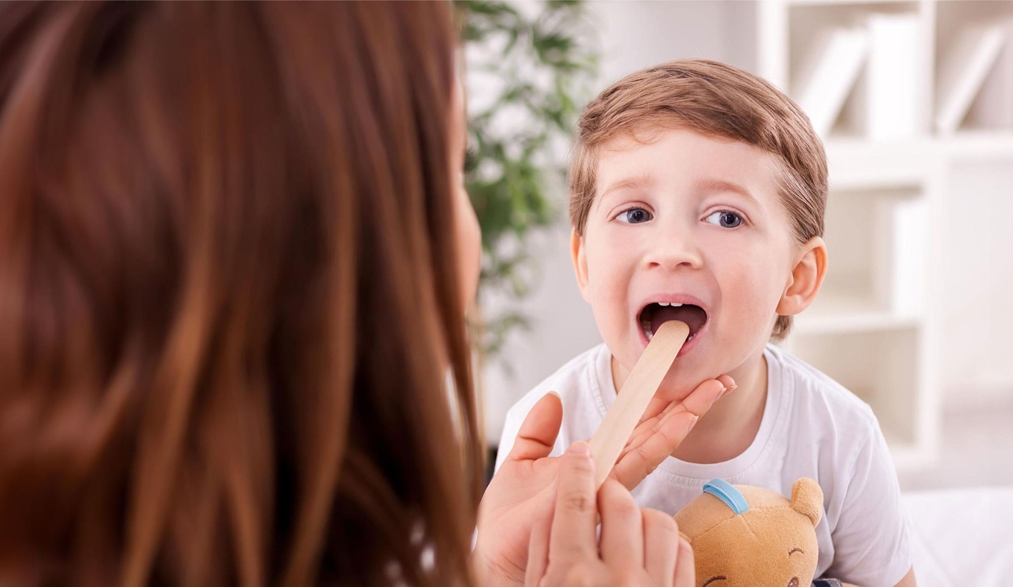 Ein Junge bekommt ein Stäbchen in den Mund und wird bei einer Kinderärztin untersucht.
